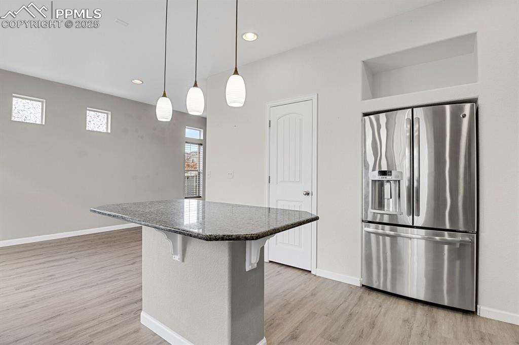Kitchen with stainless steel refrigerator with ice dispenser, decorative light fixtures, dark stone counters, a breakfast bar, and light wood-style flooring