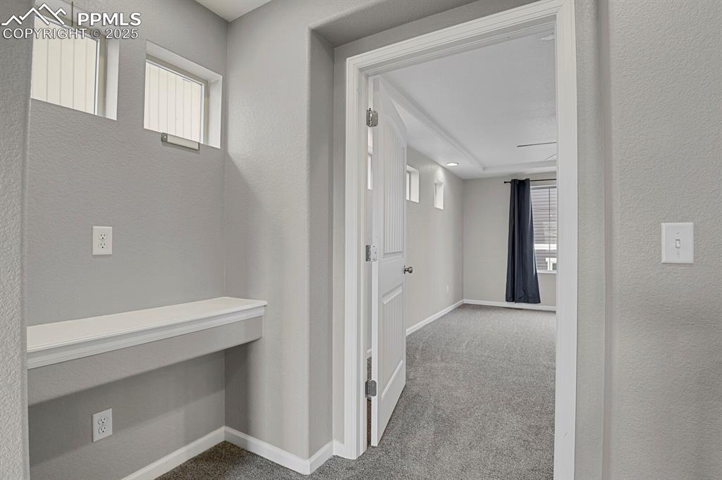Corridor featuring light colored carpet and a textured wall