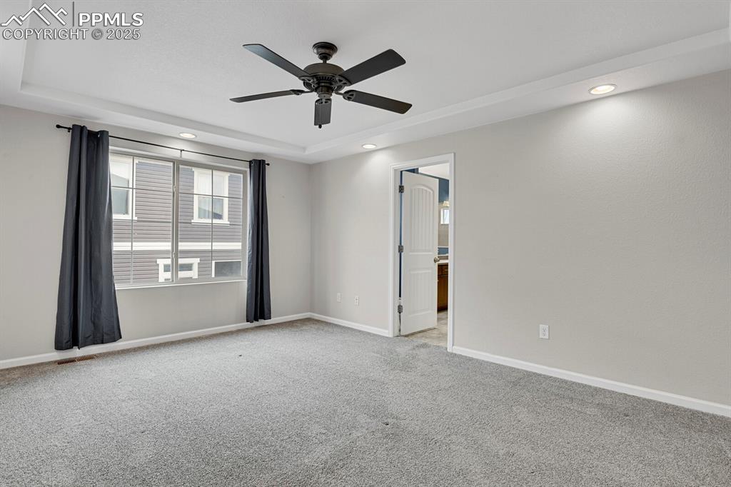 Carpeted empty room with a tray ceiling, ceiling fan, and recessed lighting