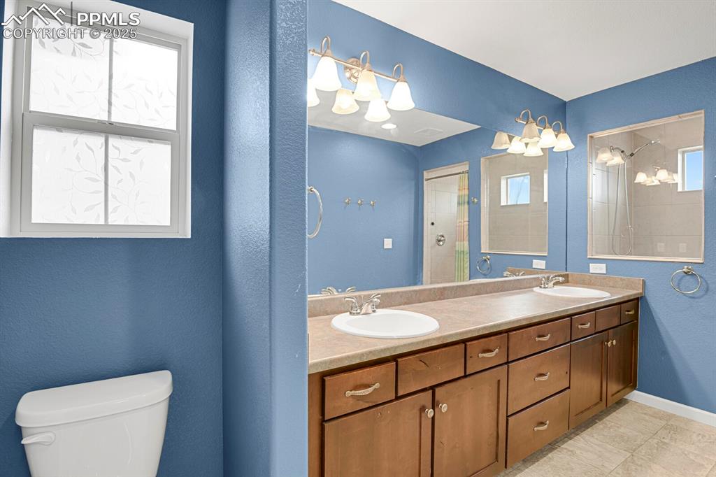 Bathroom featuring double vanity, tiled shower, a textured wall, and light tile patterned flooring
