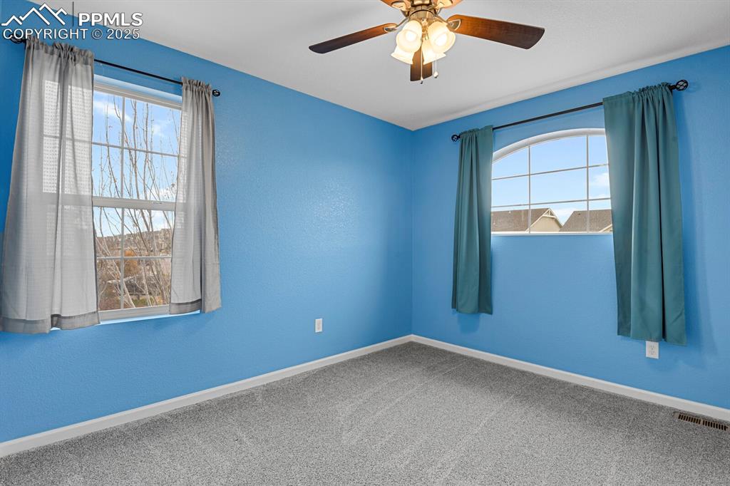 Carpeted empty room featuring a ceiling fan and a textured wall