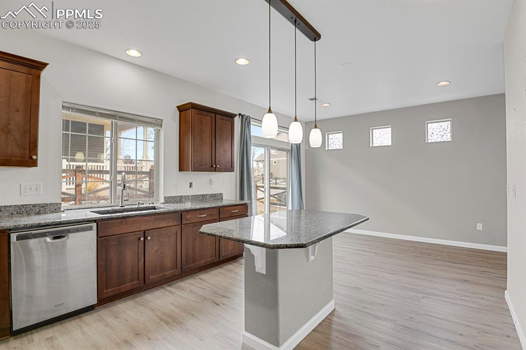 Kitchen featuring a breakfast bar, stainless steel dishwasher, decorative light fixtures, dark stone countertops, and light wood-style flooring