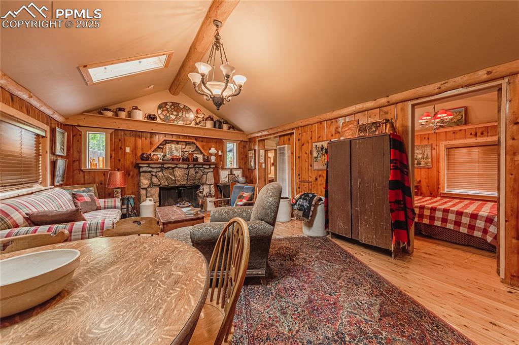 Dining area with wooden walls, a chandelier, a stone fireplace, wood finished floors, and a skylight