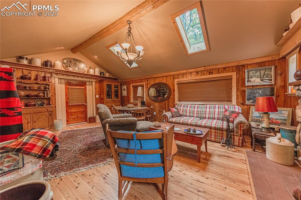 Living area featuring beamed ceiling, light wood-style flooring, a chandelier, a skylight, and high vaulted ceiling