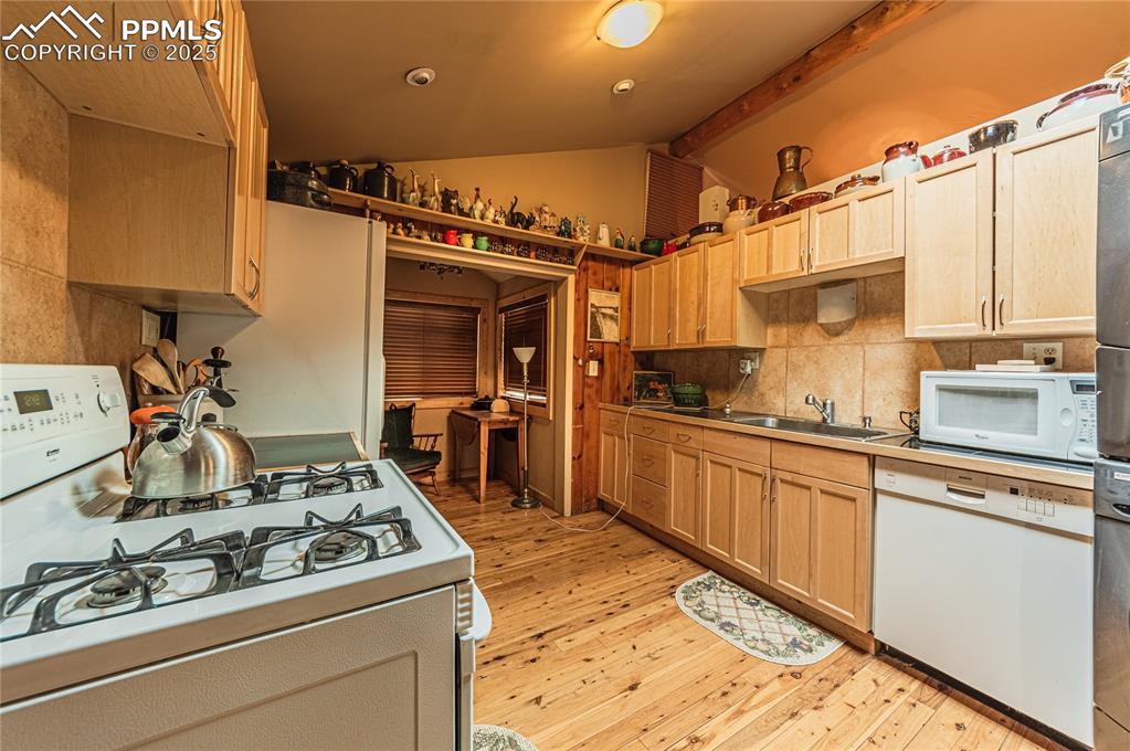 Kitchen with white appliances, light brown cabinets, light wood-style floors, and tasteful backsplash