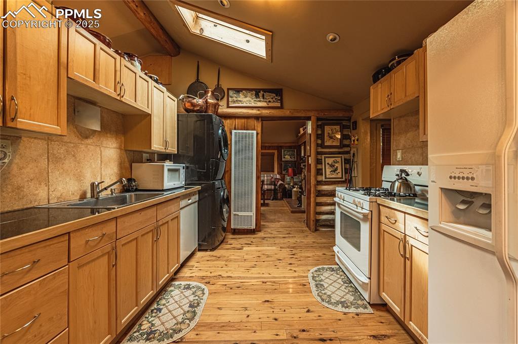 Kitchen with decorative backsplash, white appliances, a skylight, vaulted ceiling, and light wood-style floors