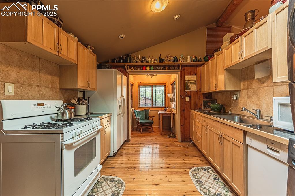 Kitchen with white appliances, lofted ceiling, backsplash, light wood-type flooring, and recessed lighting