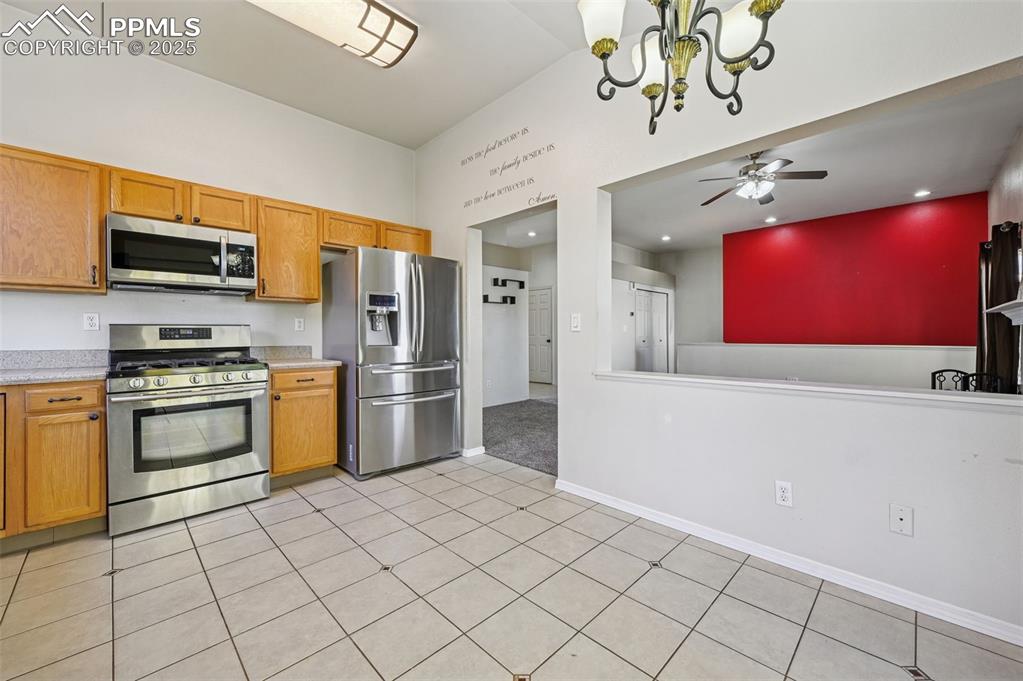 Kitchen with appliances with stainless steel finishes, a chandelier, light tile patterned floors, ceiling fan, and brown cabinetry