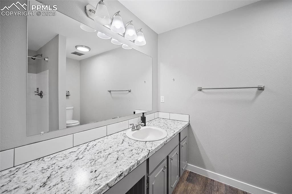 Full bath with a shower stall, vanity, dark wood finished floors, and a textured wall
