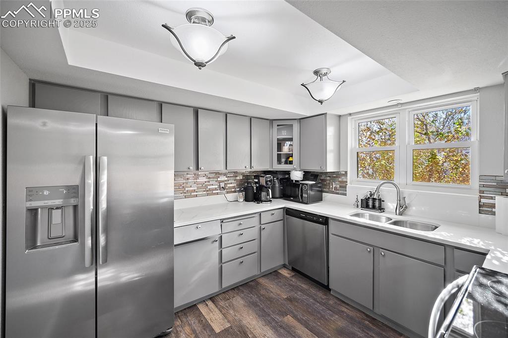 Kitchen featuring gray cabinetry, black appliances, decorative backsplash, dark wood-type flooring, and a raised ceiling