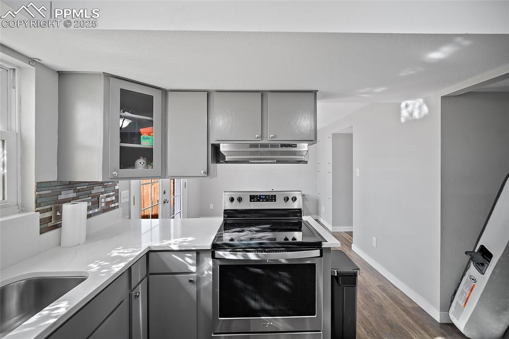 Kitchen featuring gray cabinets, stainless steel electric range, glass insert cabinets, dark wood-style floors, and backsplash