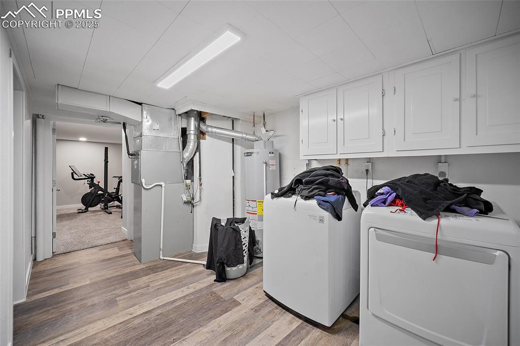 Laundry room featuring light wood-style floors, heating unit, cabinet space, gas water heater, and washing machine and dryer
