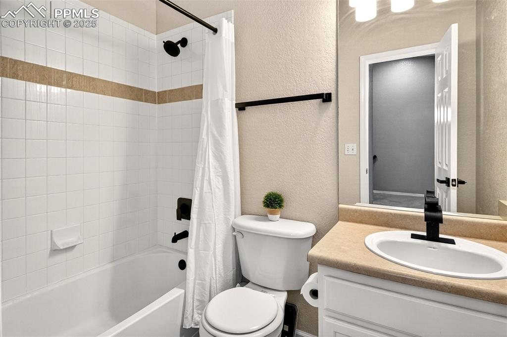 Full bathroom featuring a textured wall, shower / bath combination with curtain, and vanity