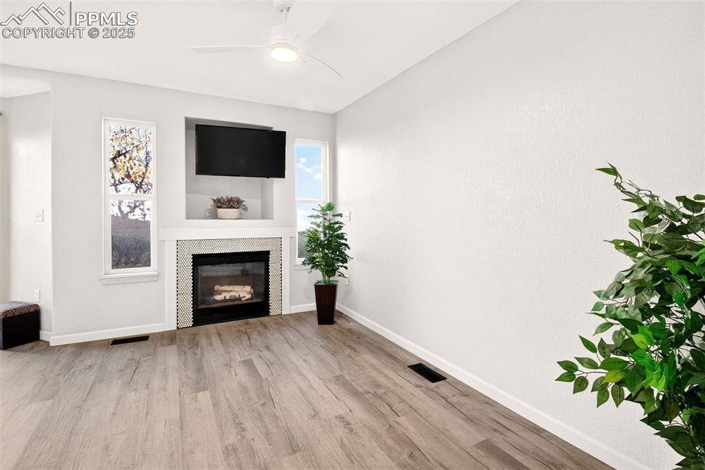 Unfurnished living room featuring wood finished floors, ceiling fan, and a tile fireplace