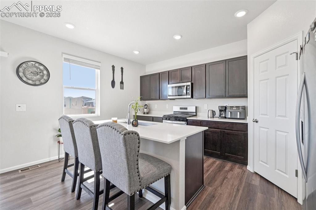 Kitchen featuring dark wood finish cabinets, stainless steel appliances, a kitchen breakfast bar, a center island with sink, and dark wood-type flooring