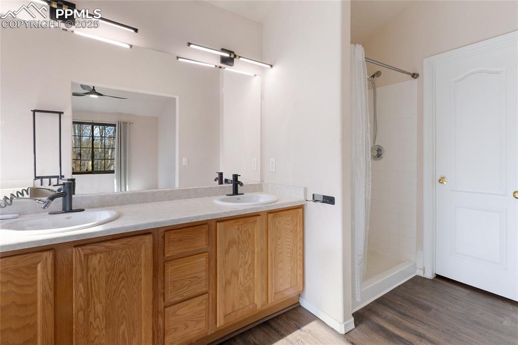 Bathroom featuring a shower stall, double vanity, dark wood-type flooring, and a ceiling fan