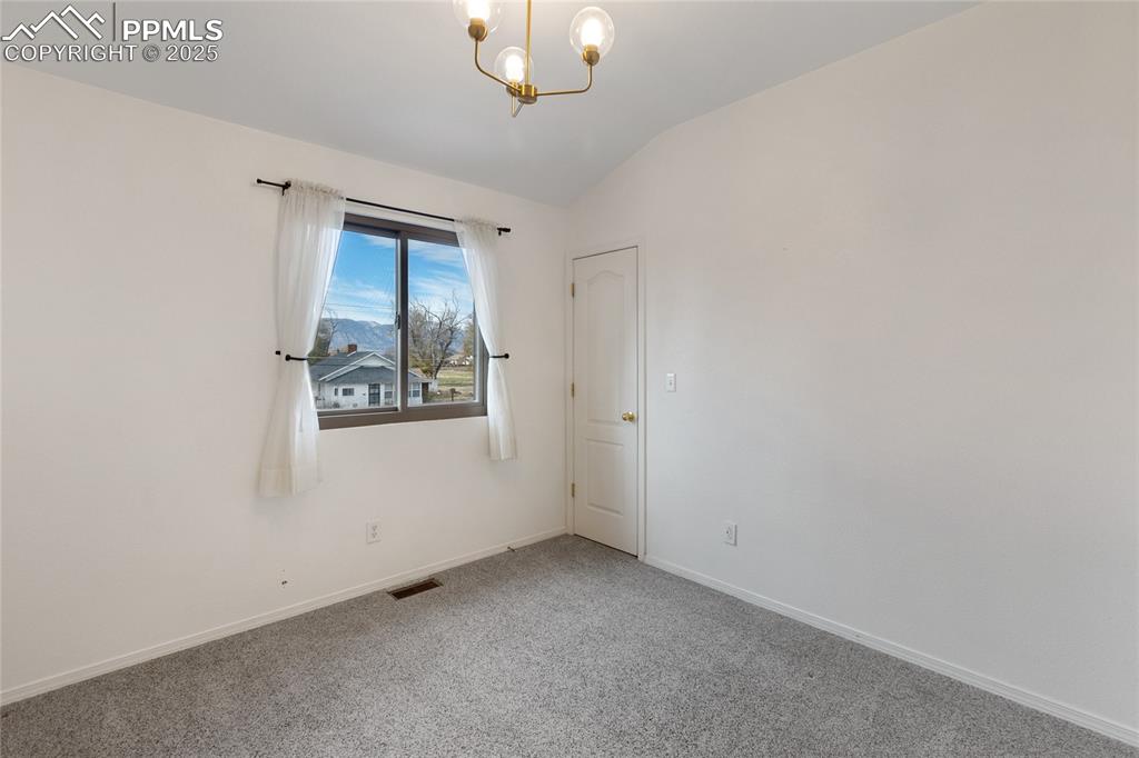 Spare room with carpet, vaulted ceiling, and a chandelier