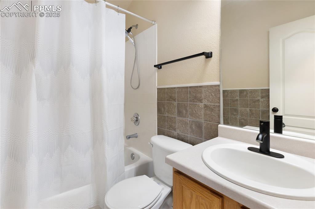 Full bathroom with vanity, tile walls, shower / tub combo with curtain, a textured wall, and wainscoting
