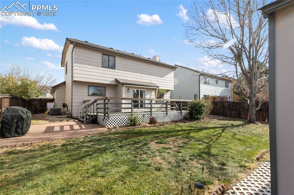 Rear view of house with a fenced backyard, a chimney, a wooden deck, and a patio area