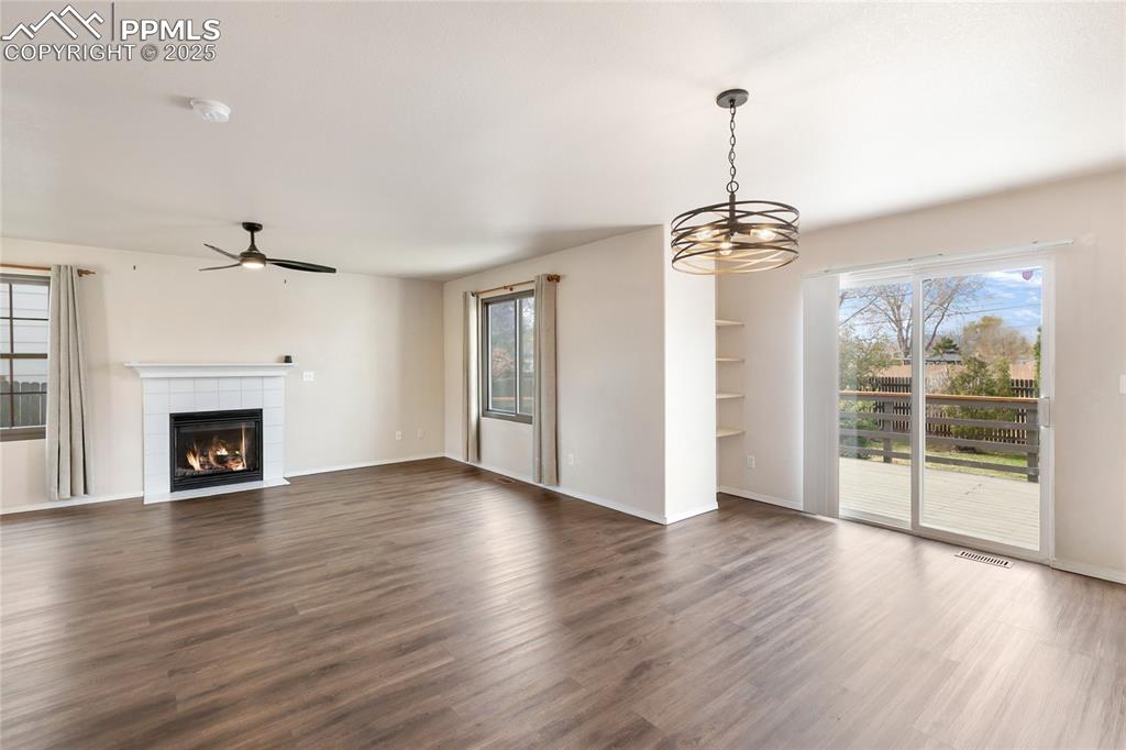 Unfurnished living room with plenty of natural light, dark wood-style flooring, a tiled fireplace, and a ceiling fan