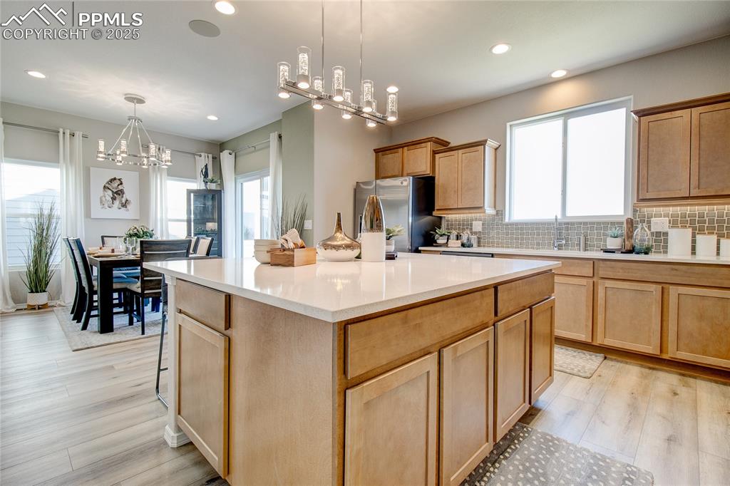 Kitchen featuring decorative backsplash, a chandelier, hanging light fixtures, a center island, and freestanding refrigerator