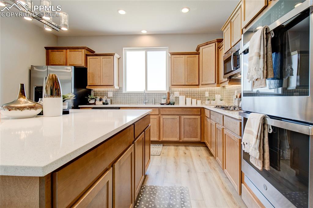 Kitchen featuring appliances with stainless steel finishes, light wood-style flooring, tasteful backsplash, light stone counters, and recessed lighting
