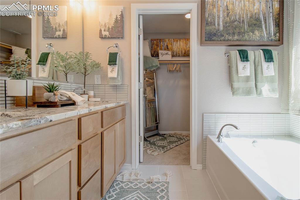 Bathroom with a garden tub, a spacious closet, vanity, and light tile patterned floors