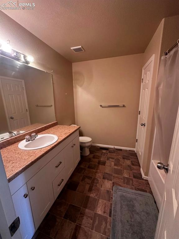 Bathroom with vanity, a textured ceiling, curtained shower, and stone finish floors