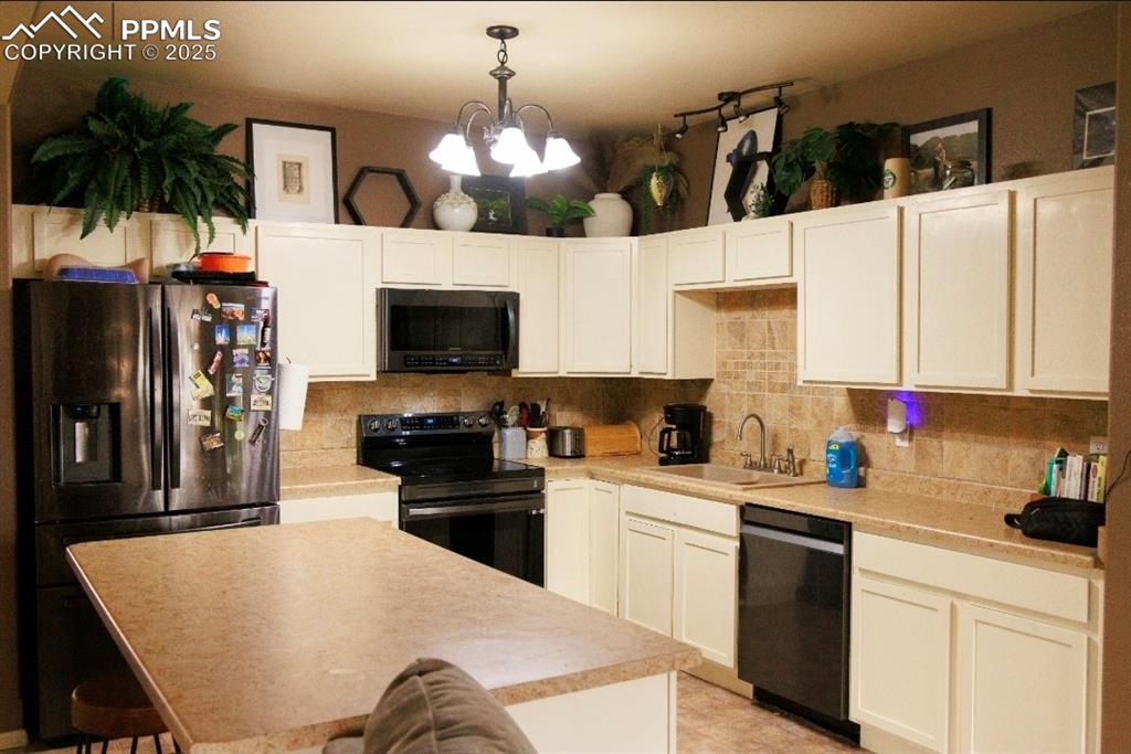 Kitchen featuring black appliances, decorative backsplash, light countertops, a breakfast bar area, and hanging light fixtures