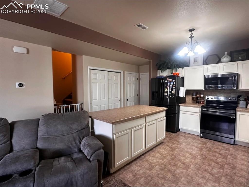 Kitchen with electric range oven, white cabinets, black refrigerator with ice dispenser, and open floor plan