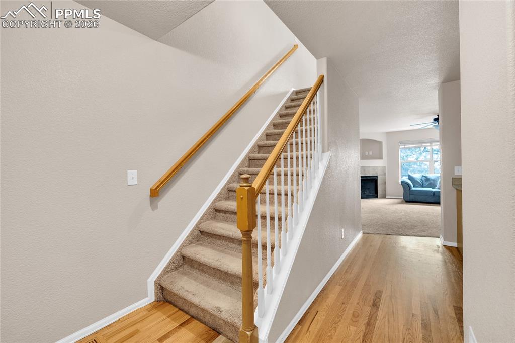 Stairway featuring wood finished floors, a fireplace, a textured ceiling, a textured wall, and ceiling fan