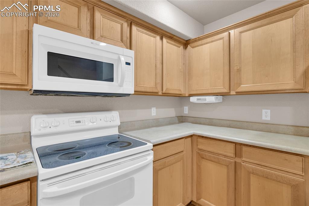 Kitchen with white appliances, light wood finish cabinetry, and light countertops