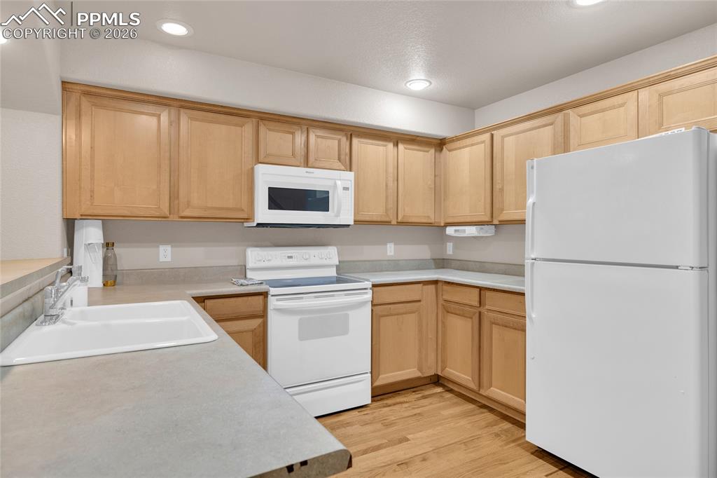 Kitchen featuring white appliances, light wood finish cabinetry, light countertops, light wood-style floors, and recessed lighting