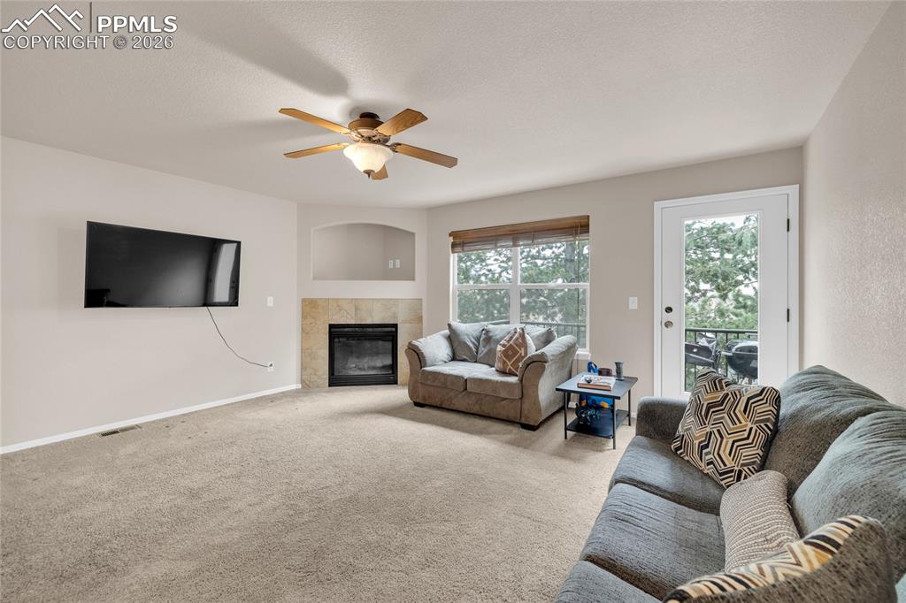 Carpeted living area with ceiling fan, a tiled fireplace, and a textured ceiling