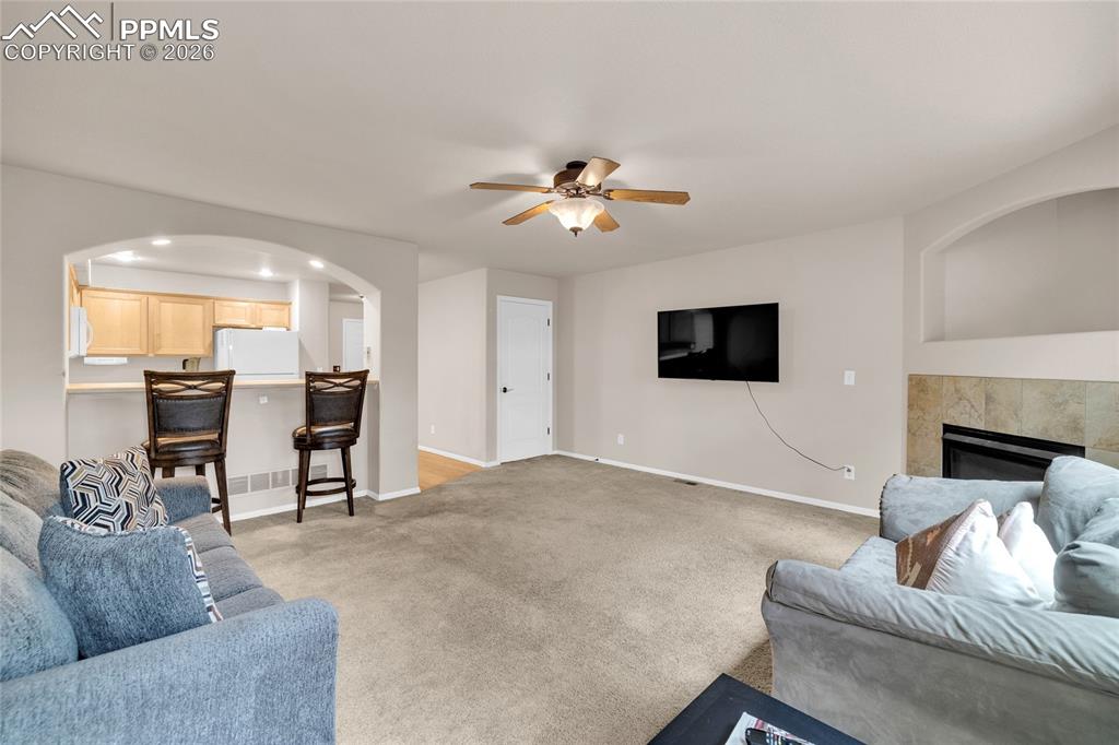 Living area with ceiling fan, light colored carpet, a tile fireplace, arched walkways, and recessed lighting