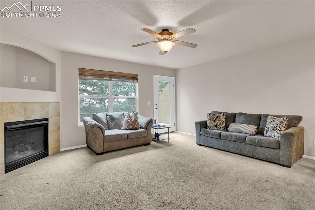 Living room featuring a fireplace, carpet, ceiling fan, and a textured ceiling