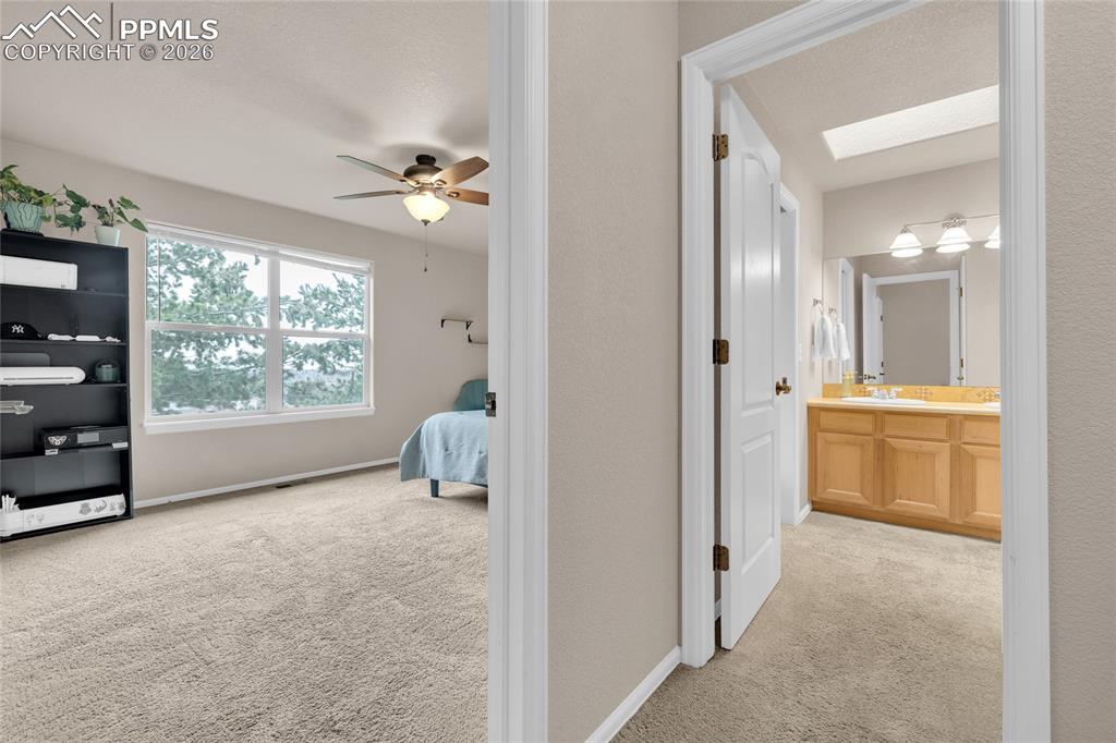 Bedroom featuring light carpet, ensuite bathroom, ceiling fan, and a skylight