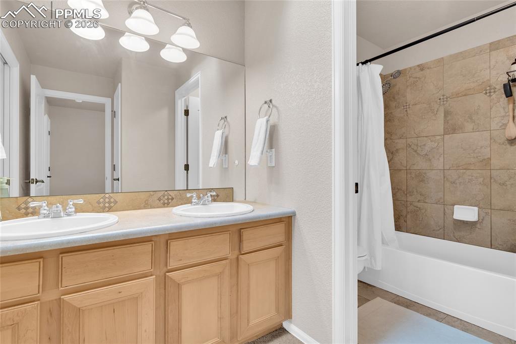 Full bath with double vanity, shower / tub combo with curtain, and a textured wall