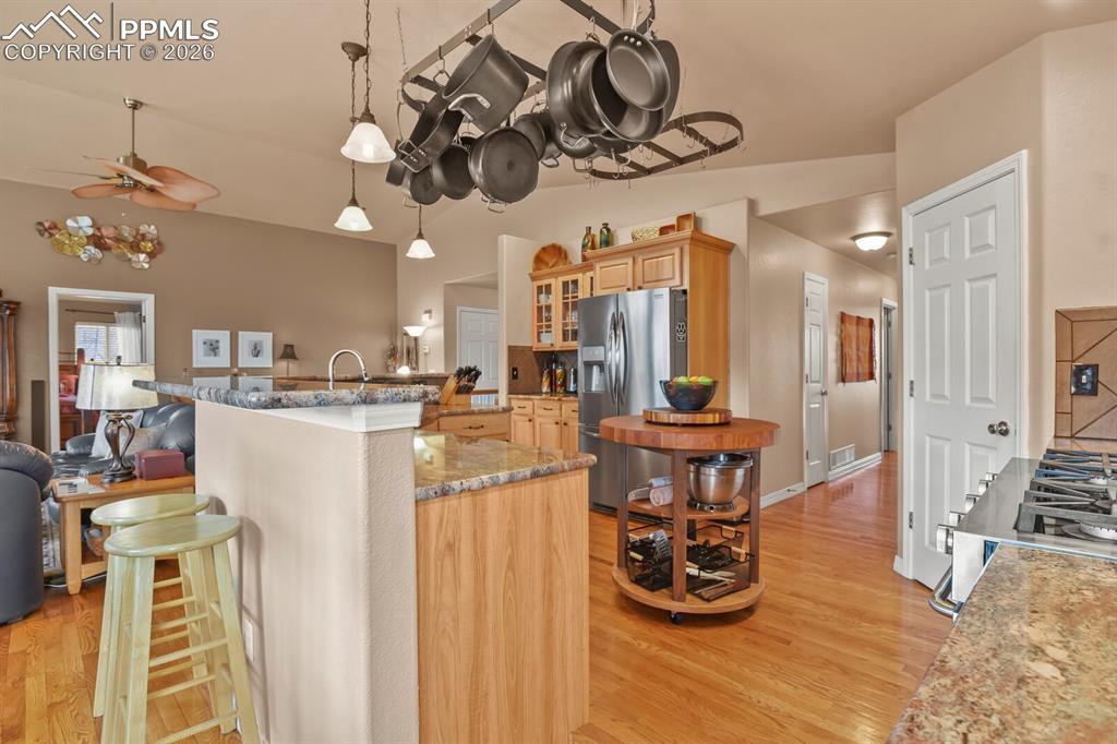 Kitchen area  featuring light wood finish cabinets some with glass doors, granite countertops, stainless steel appliances, and hardwood floors and breakfast bar. 