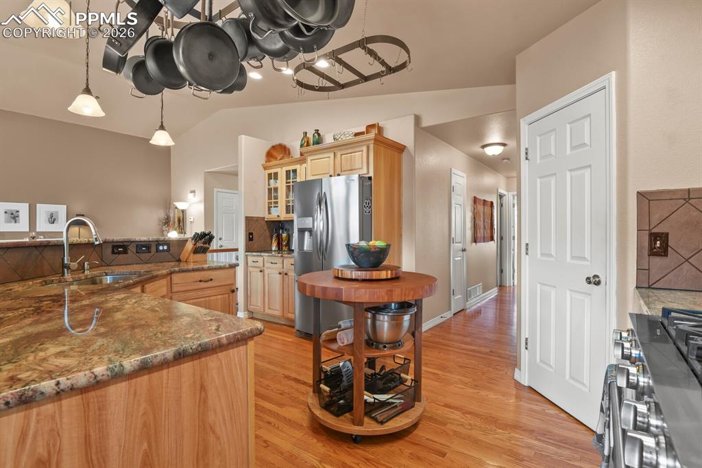 Kitchen with dark stone counters, glass fronted cabinets, stainless steel appliances, vaulted ceiling, and light wood-type flooring