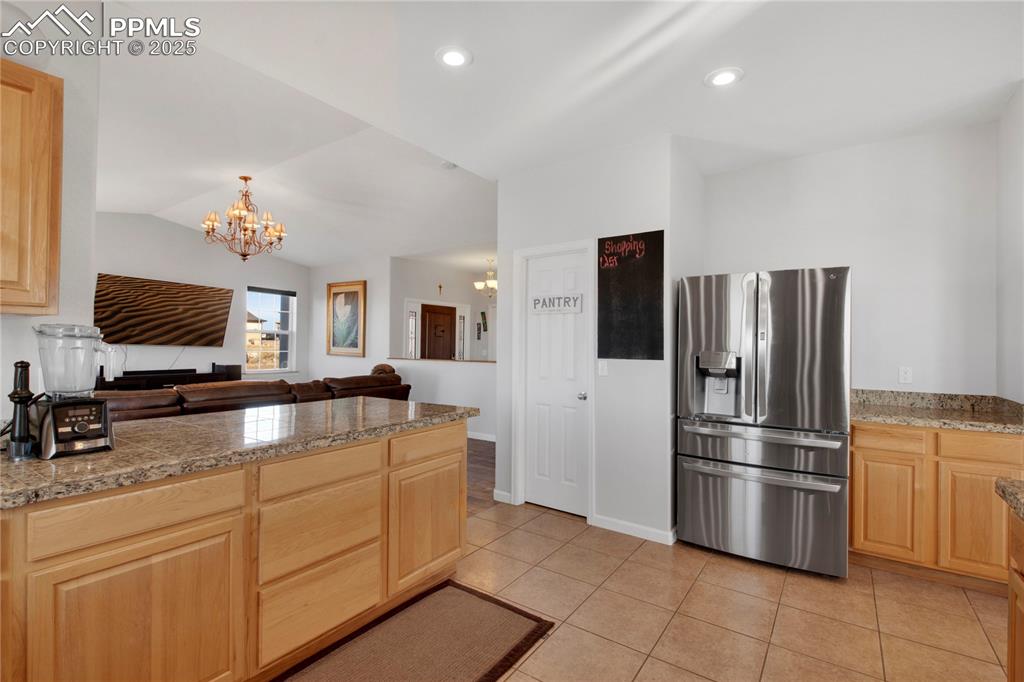 Kitchen featuring stainless steel refrigerator with ice dispenser, tile counters, a chandelier, light brown cabinets, and lofted ceiling