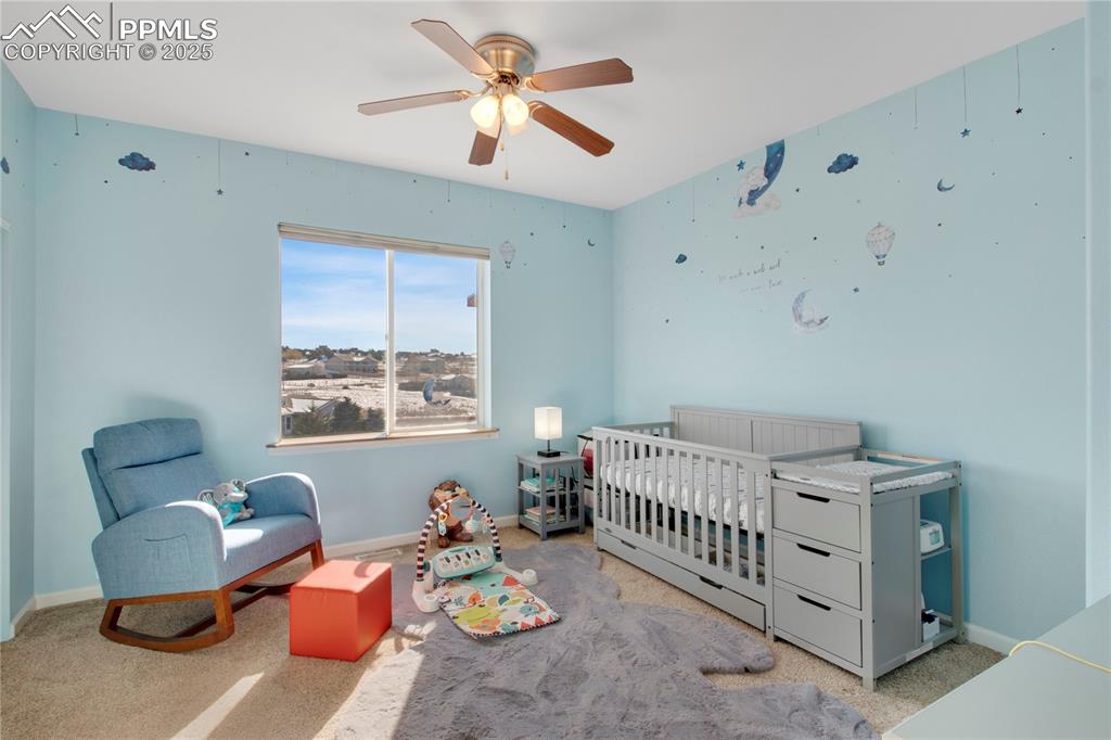 Carpeted bedroom with a crib, baseboards, and ceiling fan