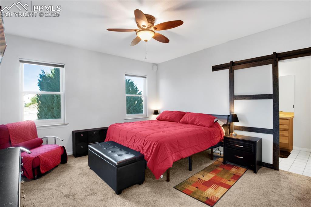 Carpeted bedroom with a barn door, ensuite bath, a ceiling fan, and baseboards