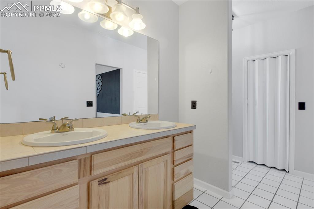 Bathroom with double vanity, tile patterned flooring, and baseboards