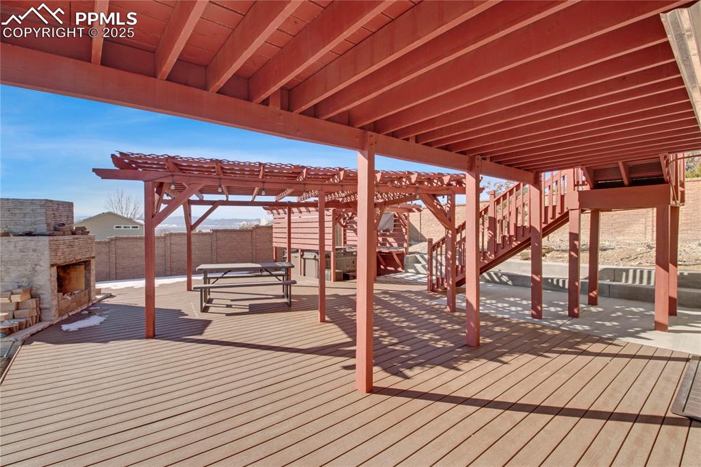 Wooden deck with a pergola, an outdoor brick fireplace, and a patio