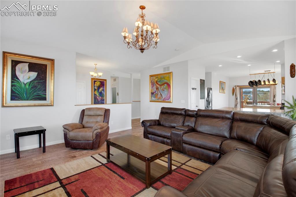 Living area with a chandelier, lofted ceiling, wood finished floors, baseboards, and recessed lighting