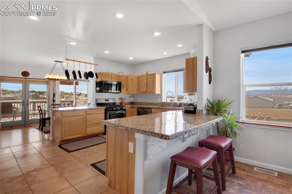 Kitchen featuring stainless steel appliances, tile countertops, light brown cabinets, a breakfast bar, and a peninsula
