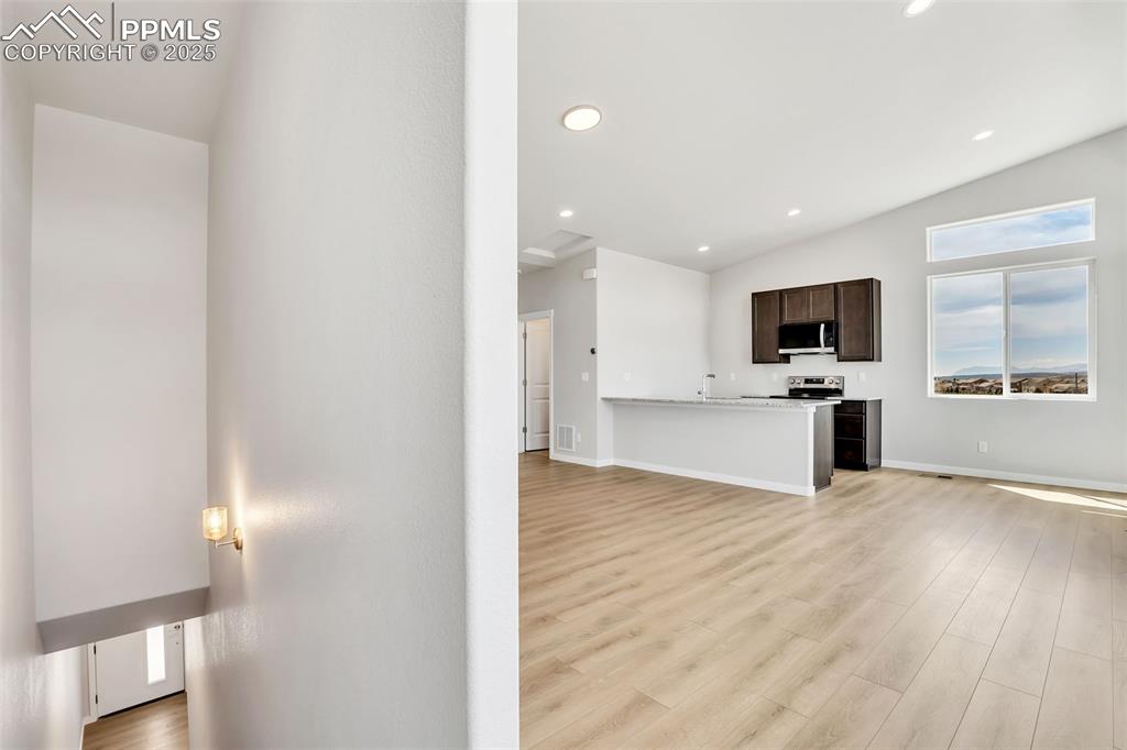 Unfurnished living room featuring lofted ceiling, baseboards, recessed lighting, and light wood-style floors