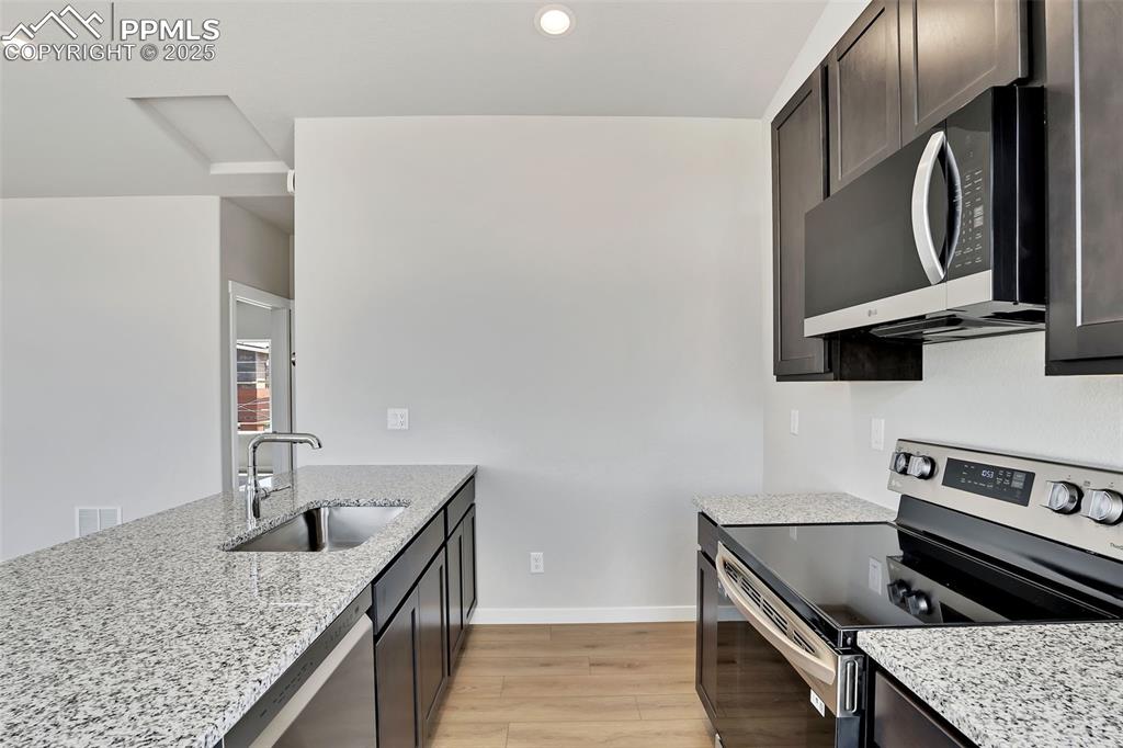 Kitchen featuring stainless steel appliances, a sink, light wood-style floors, light stone countertops, and baseboards