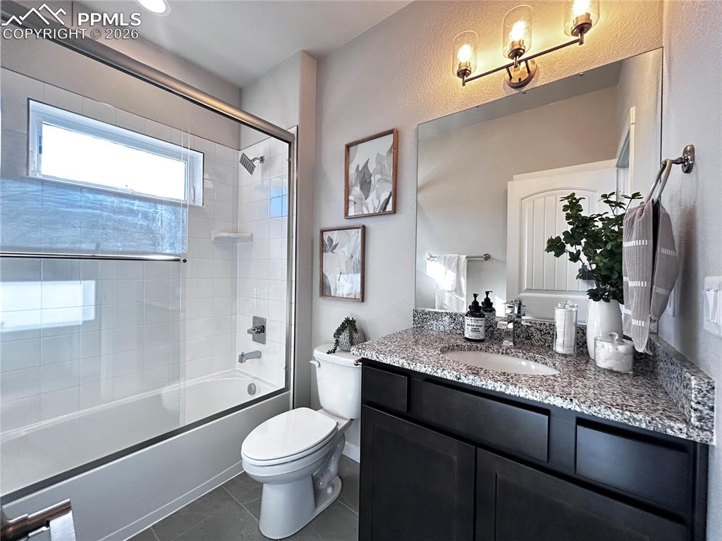 Bathroom with vanity, combined bath / shower with glass door, and dark tile patterned floors
